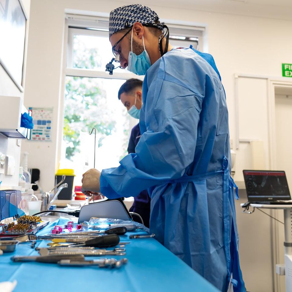 Dr George Karageorgiou in a surgical gown preparing the implant instruments, with the patient's 3D implant plan on a laptop behind him